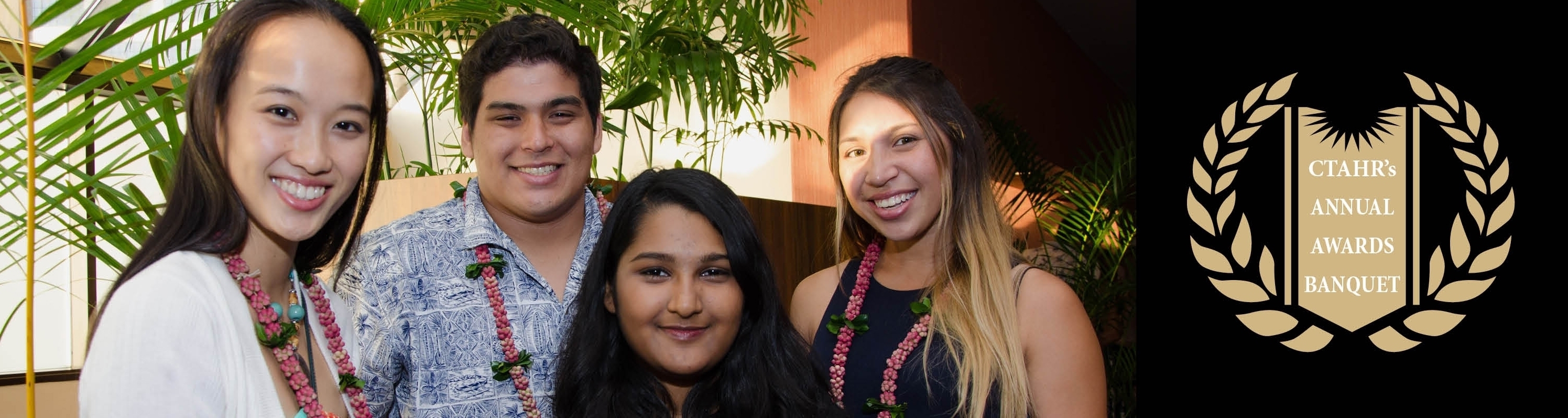 four smiling student next to CTAHR Banquet mark
